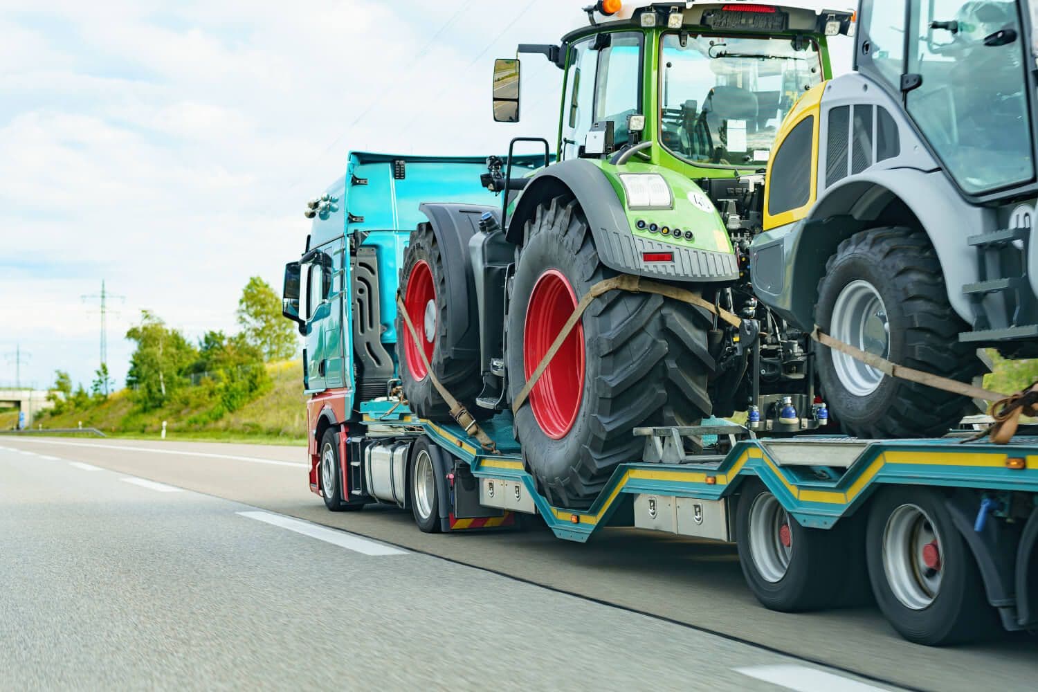 Semi-truck hauling large agricultural tractors on a flatbed trailer along a highway